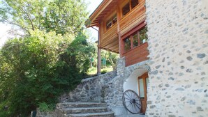 Un bâtiment rustique en pierre, avec un étage supérieur en bois, une brouette à l’extérieur et un escalier menant à l’entrée.