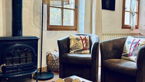 Un salon chaleureux avec un poêle à bois noir, deux fauteuils en cuir, une table basse en bois et un lampadaire à abat-jour en fibres tressées.