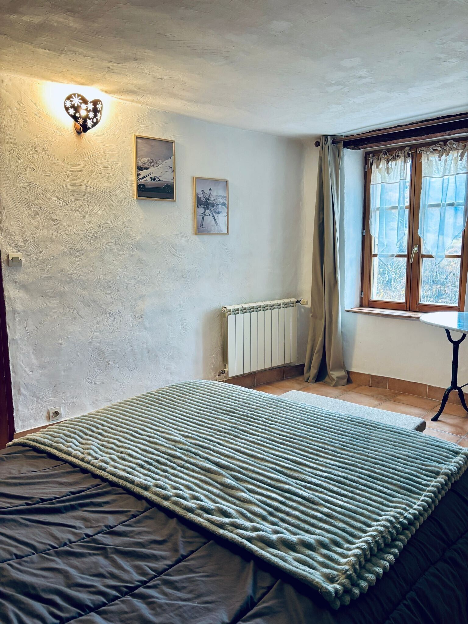 Een slaapkamer met een bed, een radiator, een raam met gordijnen en foto's aan de muur.