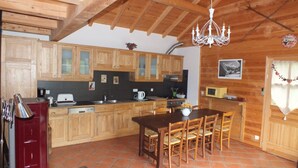 Une cuisine avec des meubles de rangement en bois, une table à manger avec des chaises, un lustre et un four à micro-ondes.