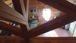 Un intérieur en bois avec un plafond en pente, un coin cuisine équipé d’une cuisinière et d’un évier, et une table à manger avec des chaises.