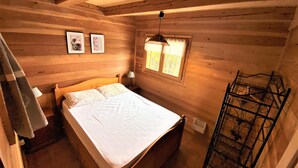 Une chambre dans une cabane en bois, avec un lit, une fenêtre avec des rideaux et une étagère fixée au mur.