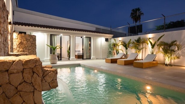 A modern pool area with a stone wall, lounge chairs, and potted plants. - Casa Kathy: Exquisite 6BR, 11 Bed & 26 Guests (Mazatlán)