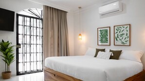 A bedroom with a large bed, a potted plant, a wall-mounted TV, and a window with curtains. - Casa Kathy: Exquisite 6BR, 11 Bed & 26 Guests (Mazatlán)