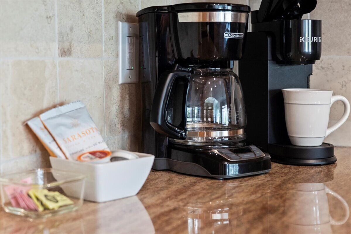 Une machine à café avec une verseuse en verre, une tasse blanche et un paquet de dosettes de café, le tout posé sur un plan de travail de cuisine.