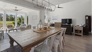 A spacious living room with a wooden dining table, white chairs, a TV, and a fireplace.