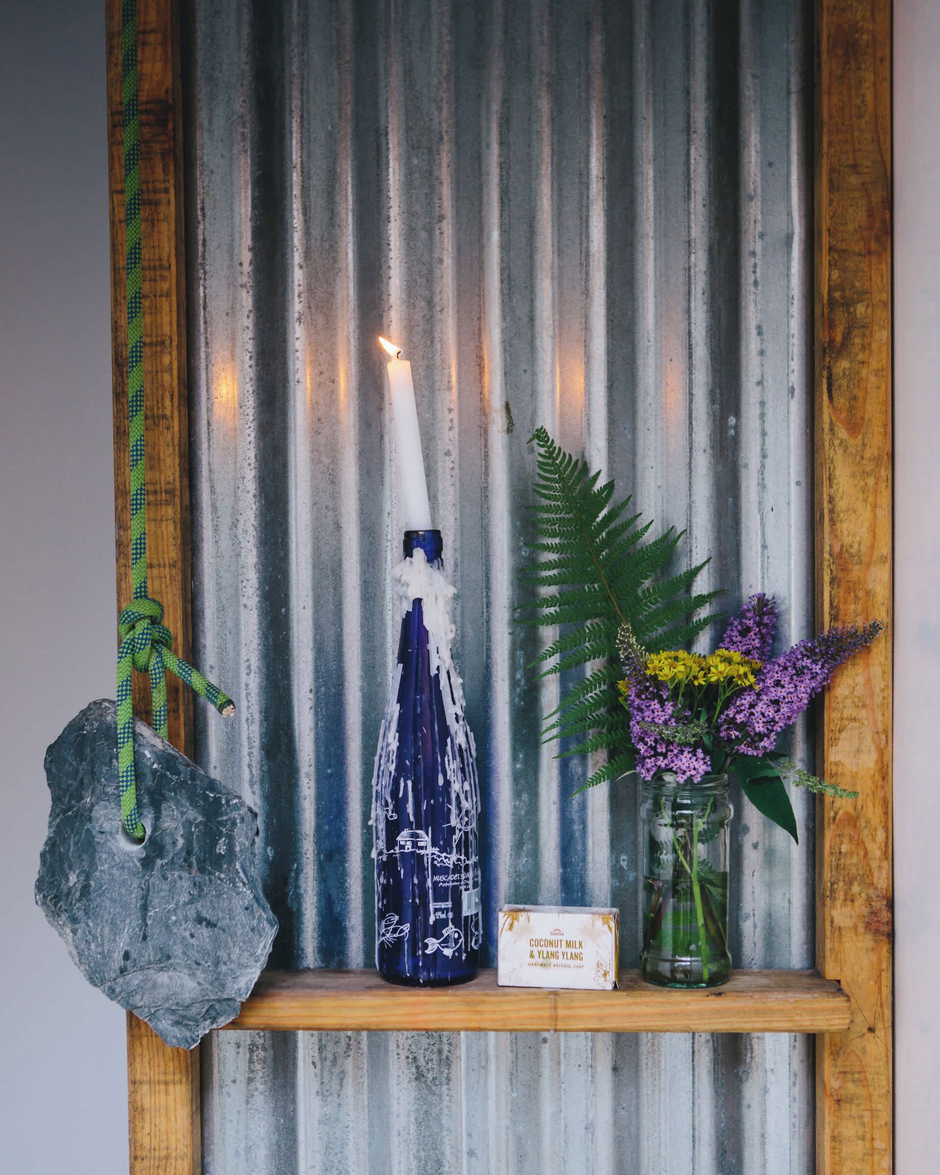 En rustik hylde med et stearinlys, en flaske og en vase med blomster.