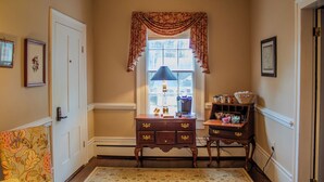 A hallway with a door, a window with a lamp, a small table with decorative items, and a patterned rug. - The Rose Room - Charming Private Studio w/ Ensuite Bath in Historic Home (Clinton)