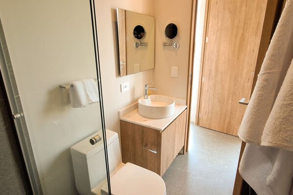 Une salle de bain moderne avec une douche à l’italienne en verre, un lavabo blanc avec un meuble-vasque en bois et des toilettes.