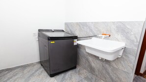 A compact washer and dryer unit with a white sink mounted on a marble wall.