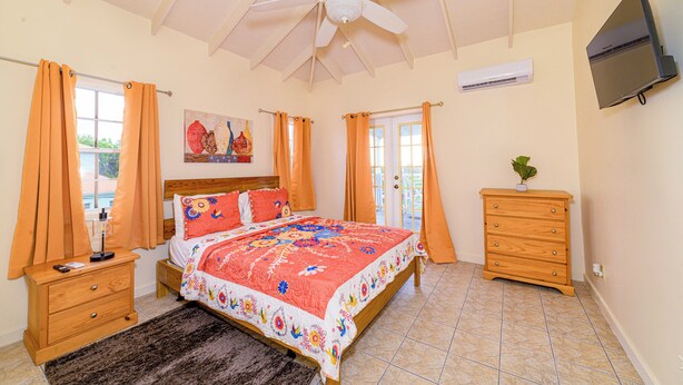 A bedroom with a bed, a nightstand, a dresser, a ceiling fan, and a TV mounted on the wall. - Charming 2-bedroom apartment with AC, WiFi in fabulous Saint John's (Saint John's)
