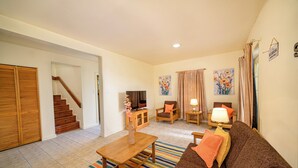 A living room with a sofa, coffee table, TV, and a staircase leading to another room. - Charming 2-bedroom apartment with AC, WiFi in fabulous Saint John's (Saint John's)