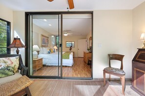 A bedroom with a sliding glass door leading to a bathroom, a wooden floor, and a bed with white bedding.