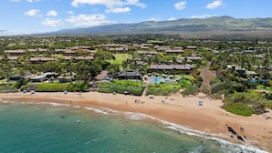 A coastal resort with multiple bungalow-style buildings, a sandy beach, and a clear view of the ocean.