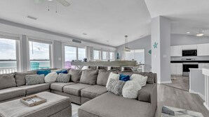 A modern living room with a large sectional sofa, a dining area, and a kitchen. - Oceanfront Paradise with Amazing Views, Hot Tub! (Surf City)