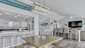 A modern kitchen with white cabinetry, a central island with stools, a dining table, and a ceiling fan. - Oceanfront Paradise with Amazing Views, Hot Tub! (Surf City)