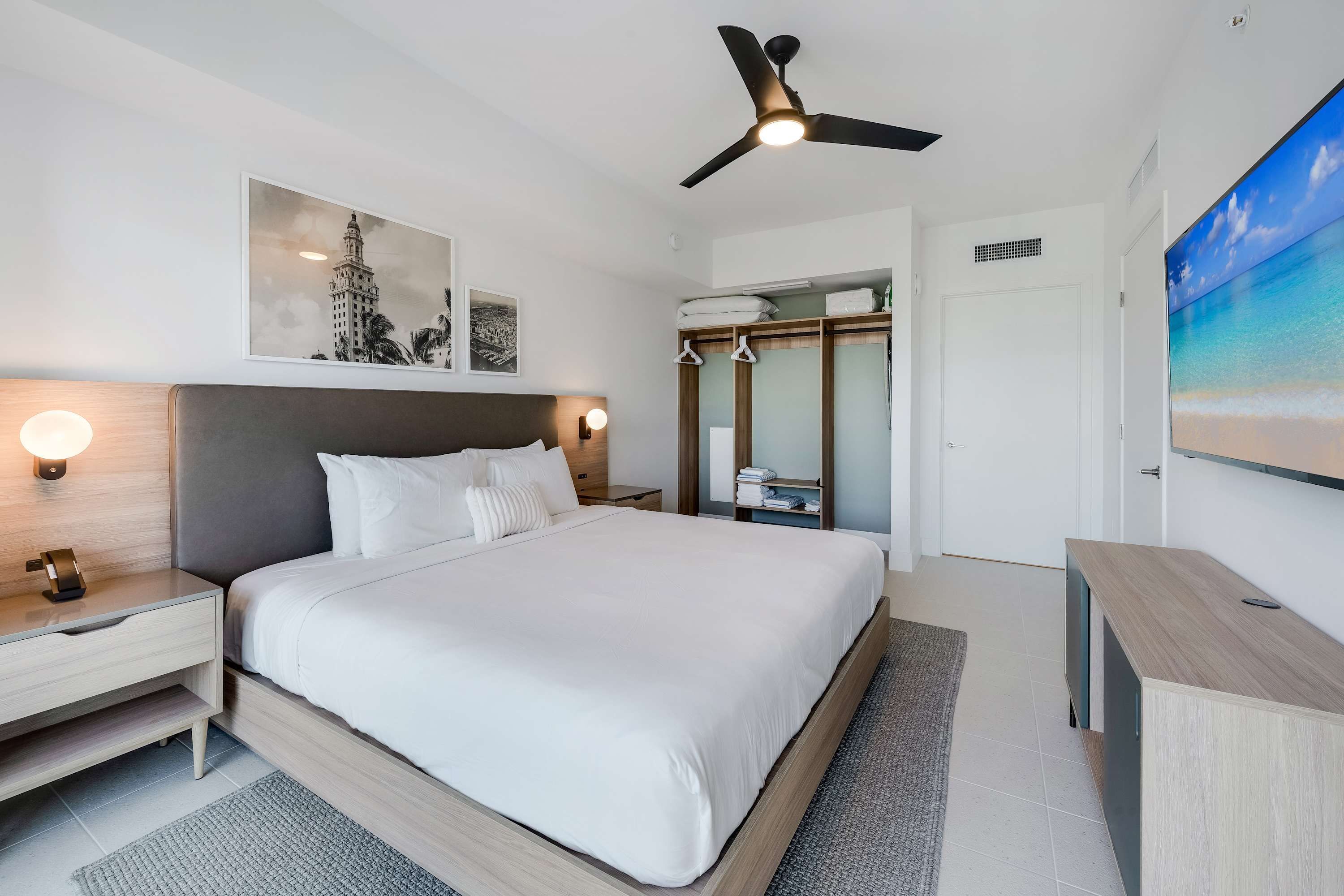 A modern hotel room with a large bed, bedside tables, a ceiling fan, and artwork on the walls.
