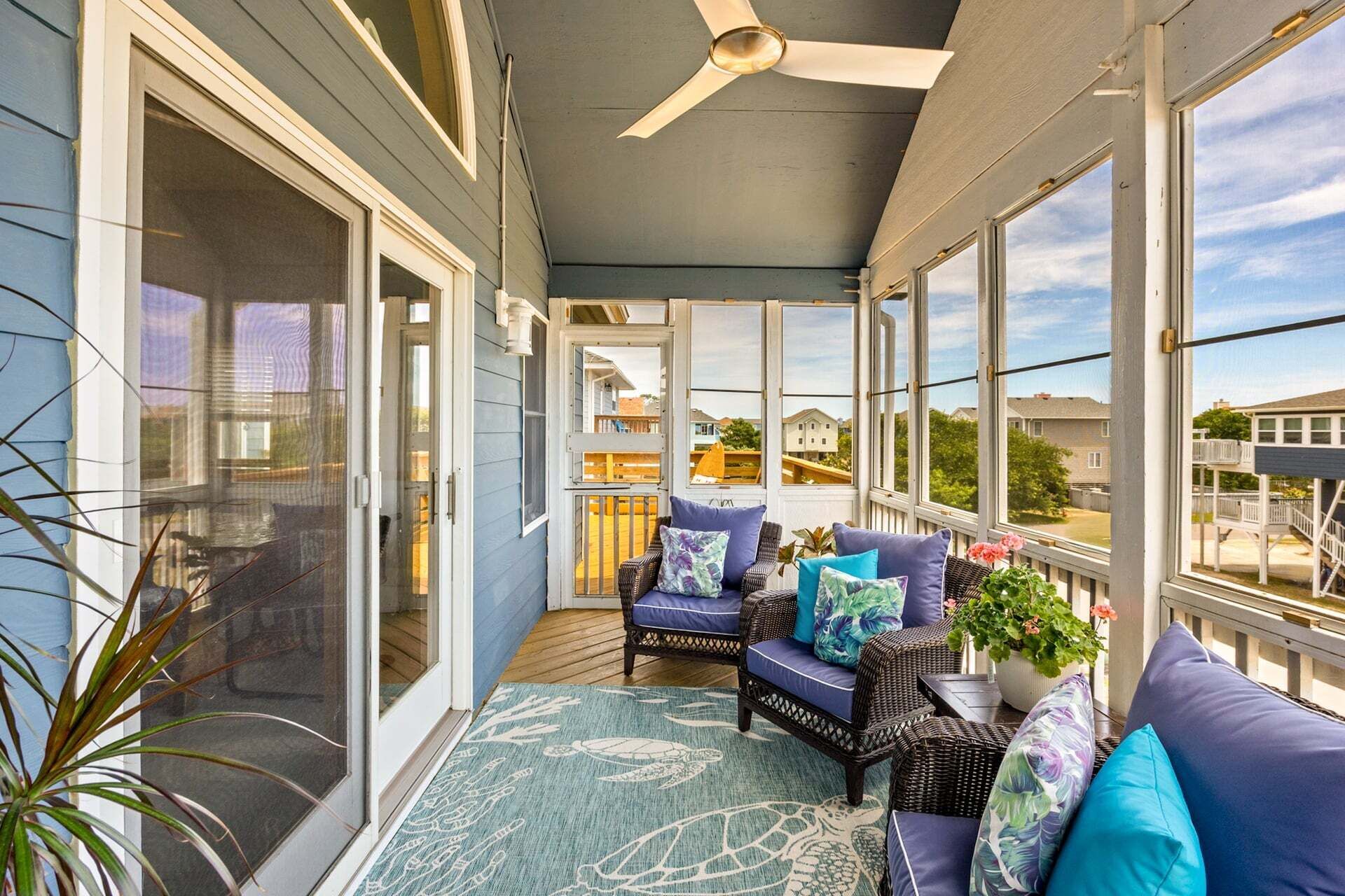 A covered porch with wicker furniture, a ceiling fan, and large windows offering a view of the neighborhood.
