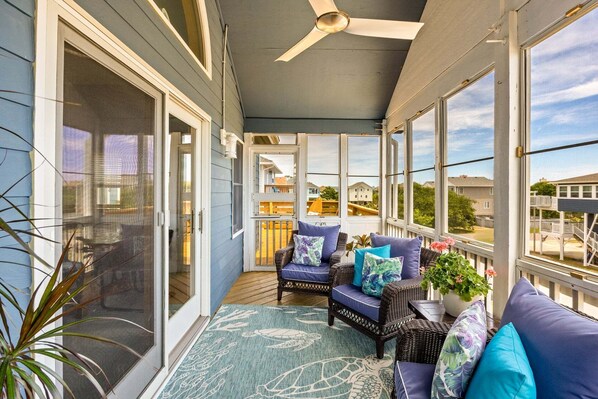 A covered porch with wicker furniture, a ceiling fan, and large windows offering a view of the neighborhood.