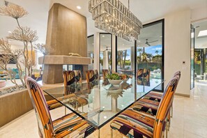 A modern dining area with a glass table, striped chairs, a large pillar, and a view of the outdoors. - Stardust - An Architectural Dream in Rancho Mirage (Rancho Mirage)