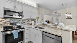 A modern kitchen with white cabinets, a stainless steel microwave, and a tiled backsplash.