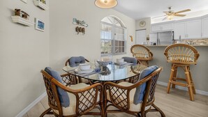 A dining area with a glass table, wicker chairs, and a ceiling fan.