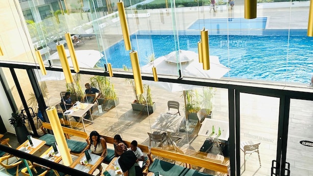 Un área de piscina interior moderna con paredes de vidrio, asientos y vistas de los edificios circundantes.