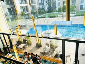 A modern indoor pool area with glass walls, seating, and a view of the surrounding buildings.