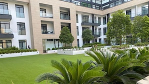 Un edificio moderno con varios balcones y un patio cuidado con césped y plantas tropicales.
