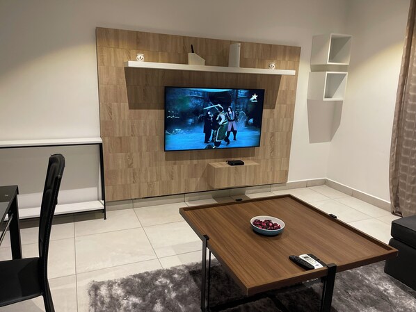 A modern living room with a flat-screen TV mounted on a wooden wall, a coffee table with a bowl and remote, and a black chair.