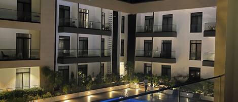 A modern building with a rooftop pool, glass railings, and multiple balconies.