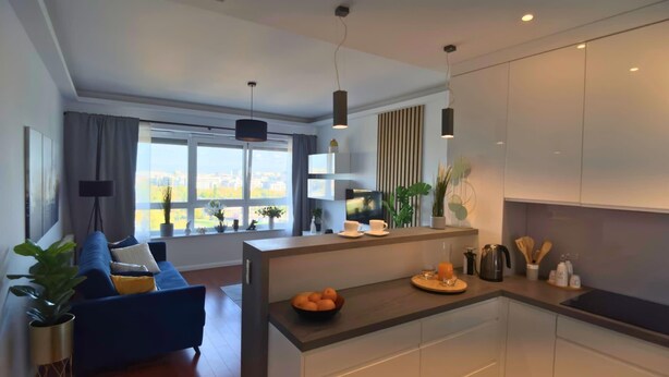 Una cocina moderna con una isla central, un área de comedor con sofá azul y un ventanal con vistas a la ciudad.