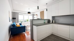 Una cocina moderna con armarios blancos, encimera gris y un sofá azul con un cojín amarillo.