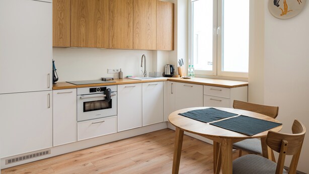 Une cuisine moderne avec des meubles en bois, un four encastré et un coin repas comprenant une table et des chaises.