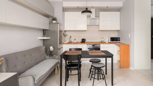 Et moderne køkken med hvide skabe, et spisebord med sorte stole og en grå sofa.