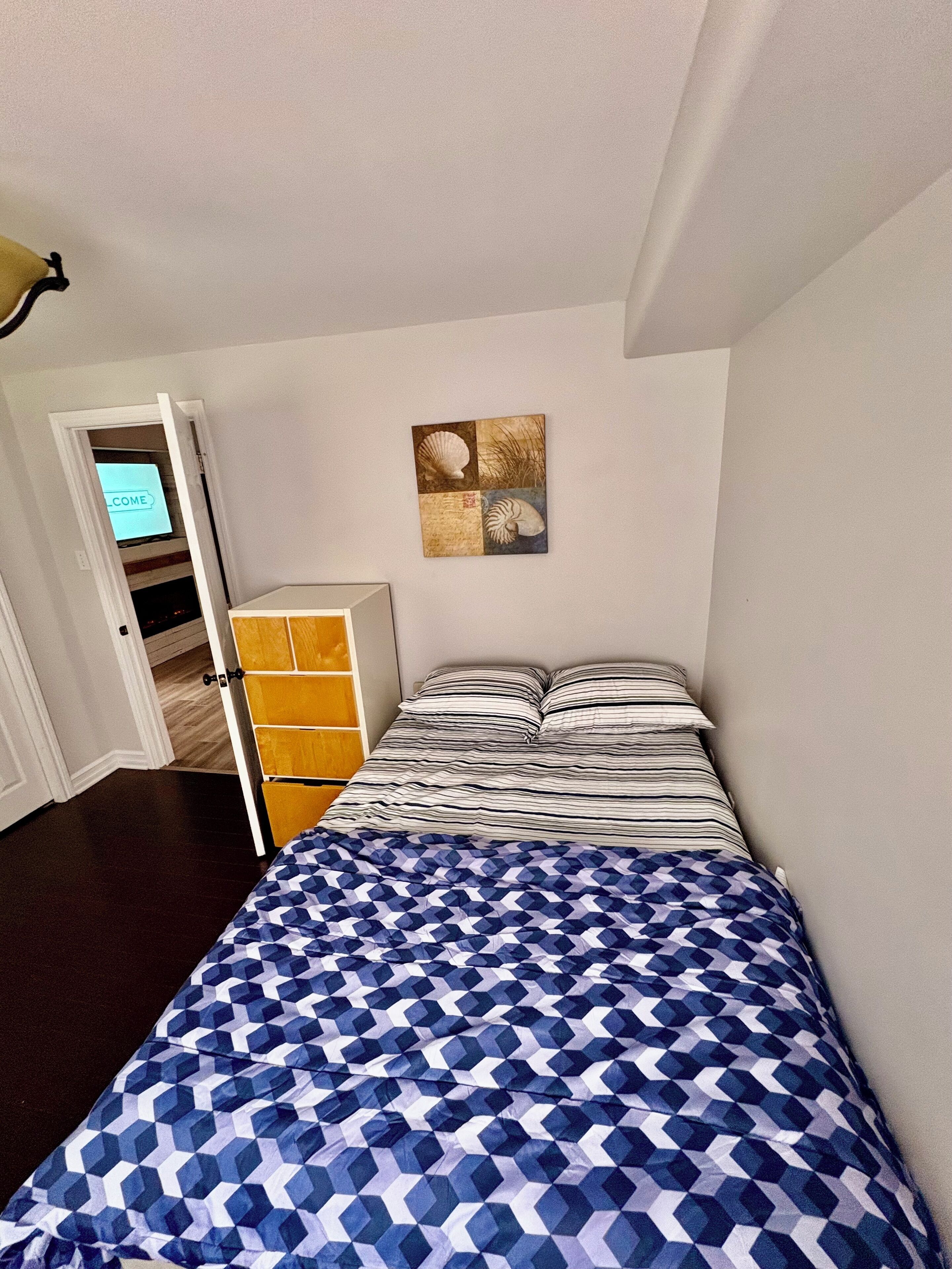 A bedroom with a bed, a dresser, and a wall-mounted artwork.