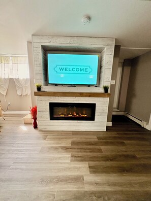 Een moderne woonkamer met een open haard, een flatscreen televisie erboven en een welkomstbord.