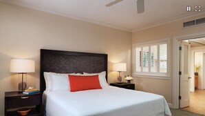 Habitación de hotel con una cama grande, dos mesitas de noche con lámparas, un ventilador de techo y vistas al exterior por una puerta.