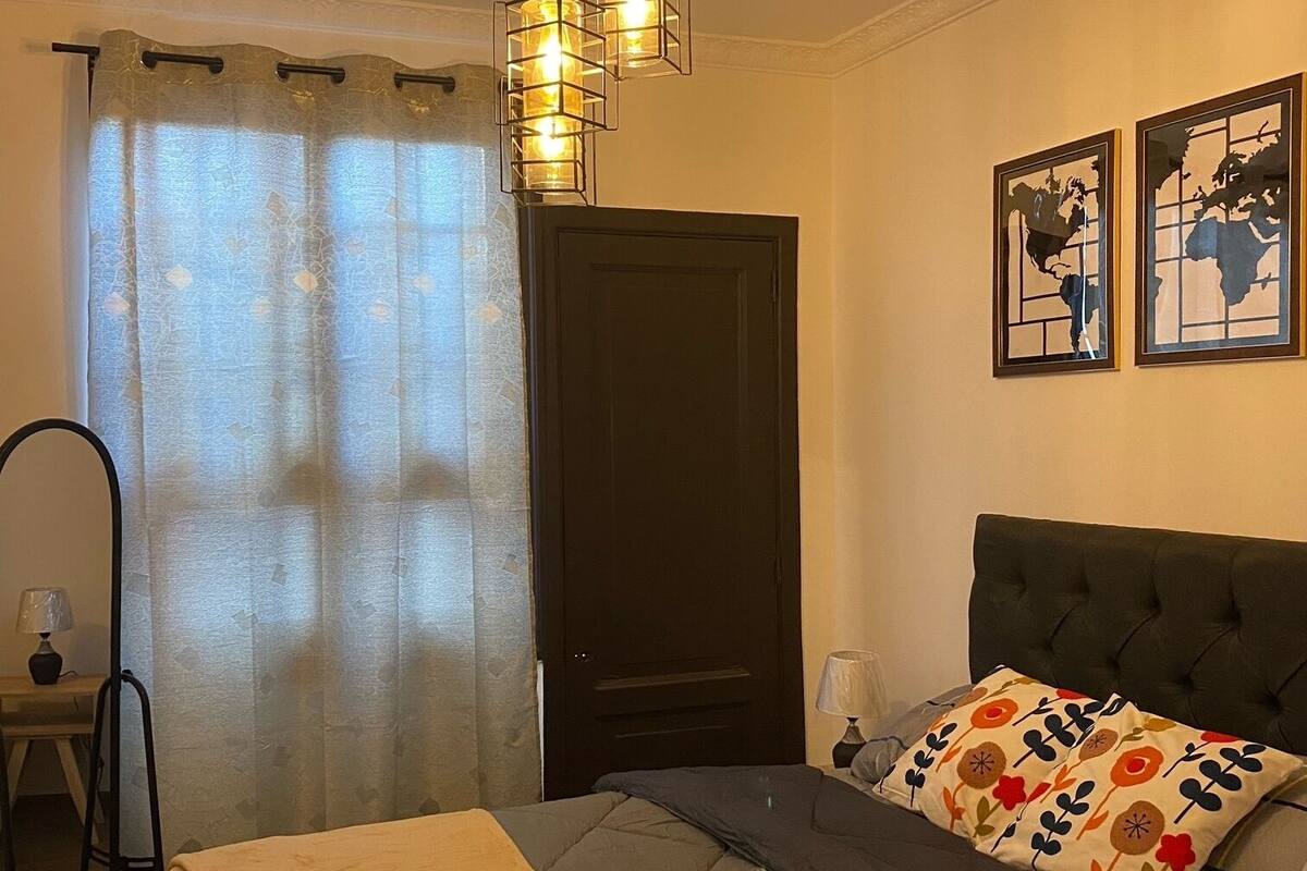 A bedroom with a bed, a desk, a chair, a door, and a ceiling light fixture.