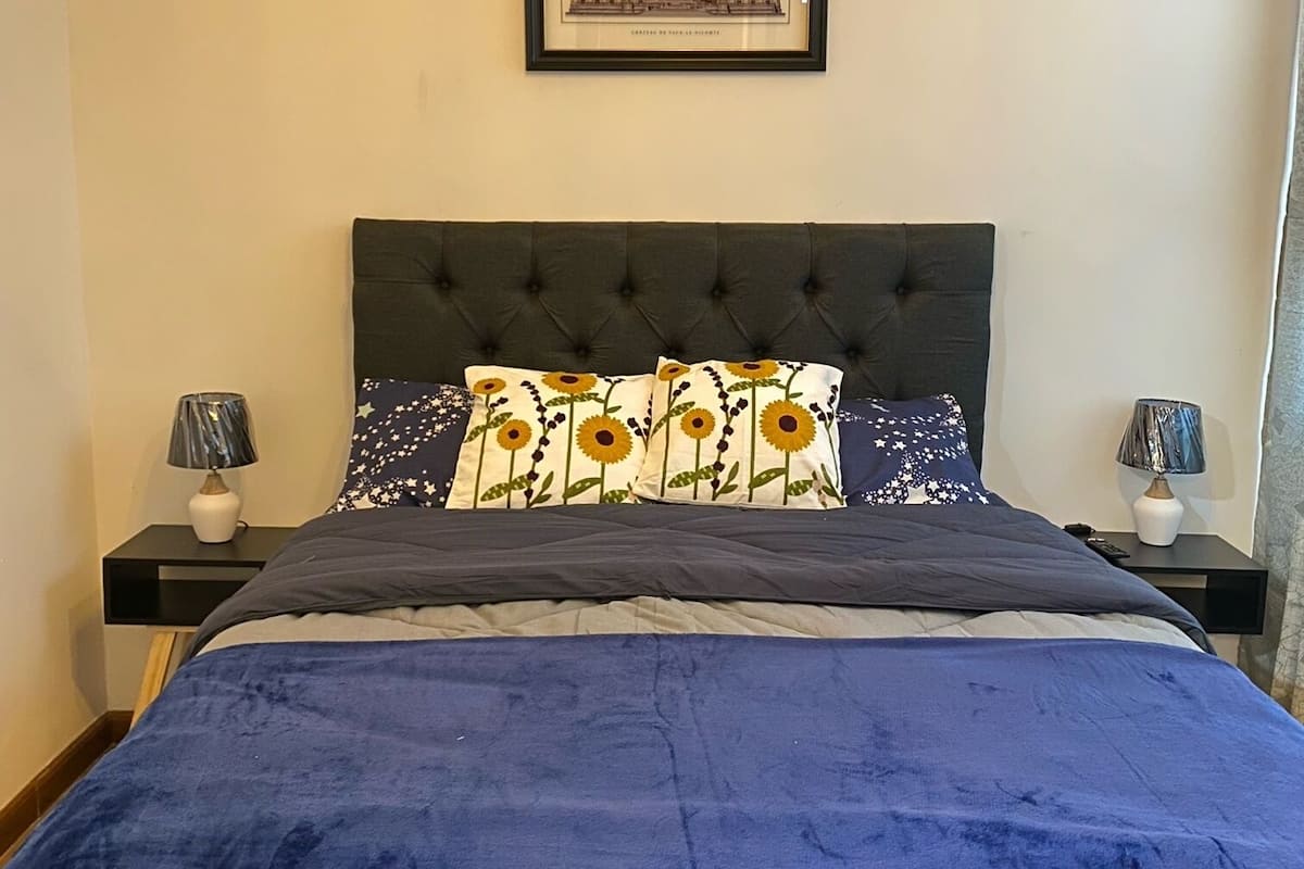 A bedroom with a large bed, a framed picture on the wall, and two bedside tables with lamps.