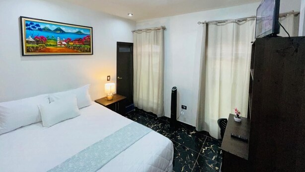 Habitación de hotel con cama, un cuadro en la pared, escritorio con lámpara y televisor sobre un mueble.