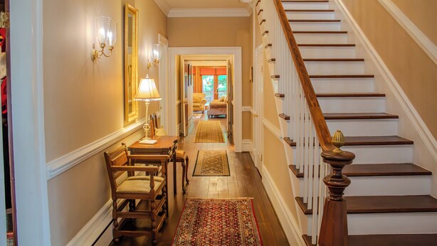 A hallway with a staircase, a dining area with chairs and a table, and a rug on the floor.