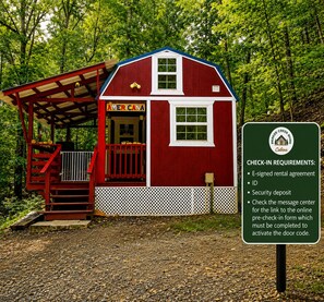 Une cabane rouge avec un porche, une affiche indiquant les conditions d’enregistrement et le logo de Parker Creek Cabins.