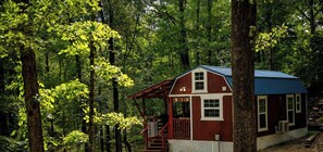 A cabin with a porch, surrounded by dense forest. - Americana Cabin (Murfreesboro)