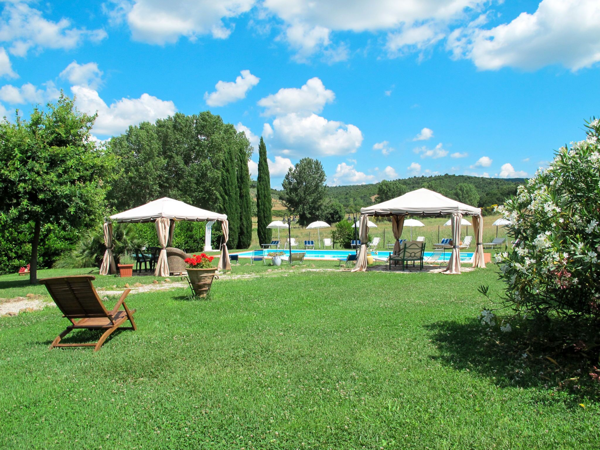 A poolside area with two gazebos, lounge chairs, and a swimming pool.