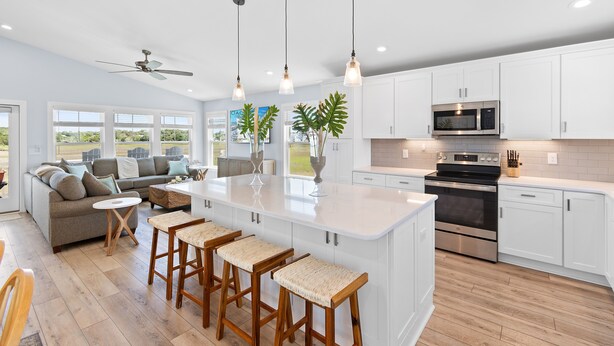 Una cocina moderna con gabinetes blancos, una isla grande con taburetes de bar, horno empotrado y microondas.