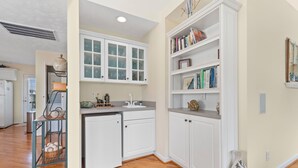 A kitchen with white cabinets, a built-in oven, and a sink. There is a bookshelf with books and decorative items.