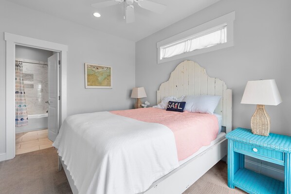 A bedroom with a bed, a nightstand, a lamp, a window, and a door leading to a bathroom.