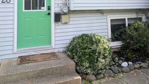 Una casa de dos pisos con una puerta verde, número 20, y un pequeño jardín delantero con un arbusto y escalones que conducen a la puerta.