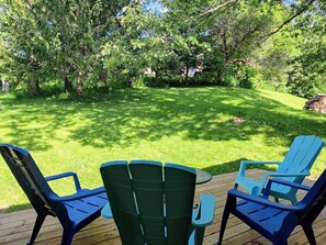 Une terrasse avec quatre chaises Adirondack et une table, entourée d’une pelouse verdoyante et luxuriante et d ’arbres.